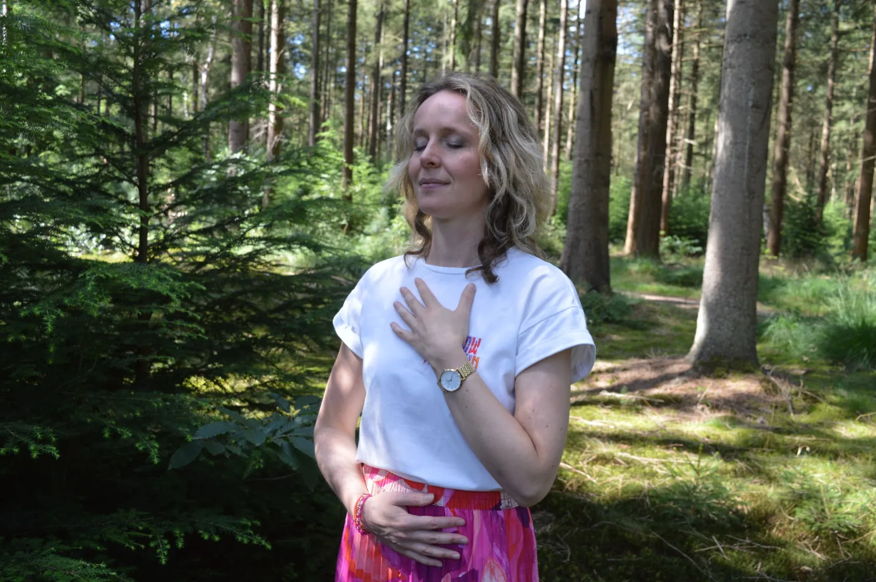 Marloes met haar handen op hart en buik in het bos